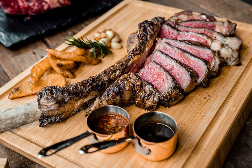 Délicieux steak Tomahawk en tranches sur une planche de bois et près à déguster. Comment cuire le parfait steak Tomahawk?