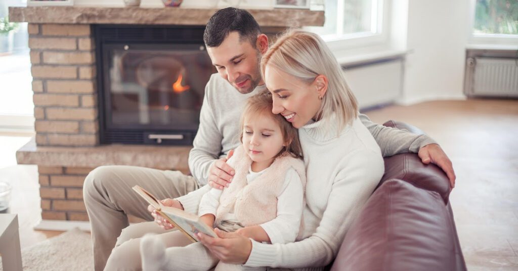 20 Activités Chaleureuses Près du foyer pour le Plaisir et la Détente en Hiver - un couple et leur petite fille lisent un livre au coin du feu