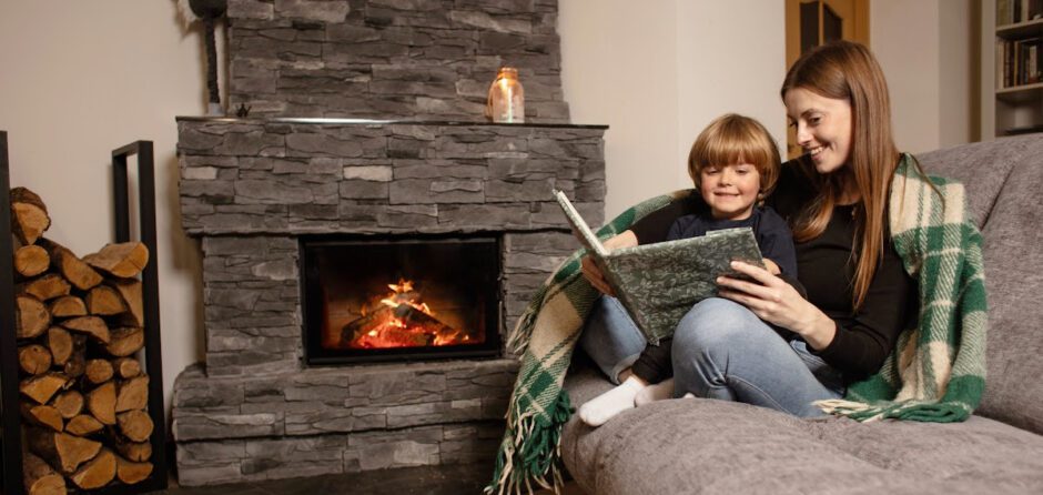 A mother and son cuddle by the fireplace reading a book