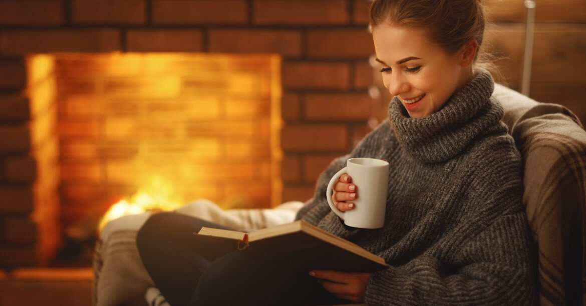 Une femme lit un livre en buvant une boisson chaude au coin du feu