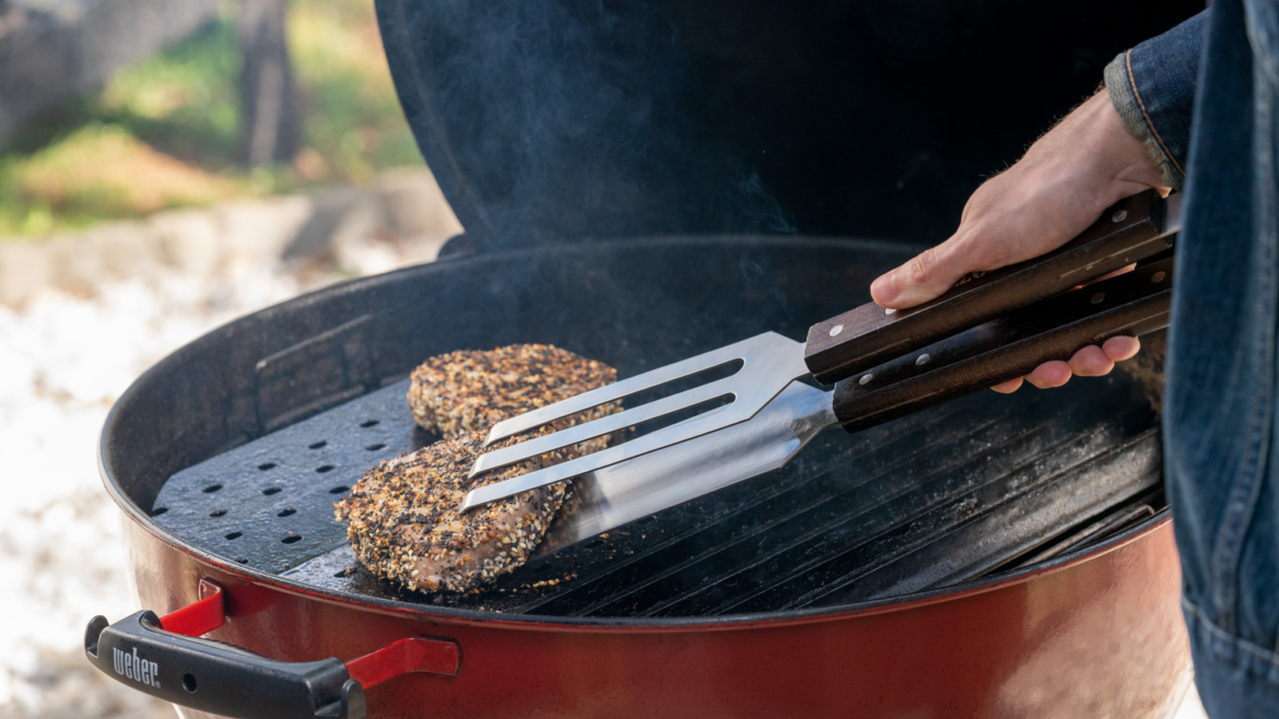 Une viande est en train d'etre tourner par des pinces sur un barbecue