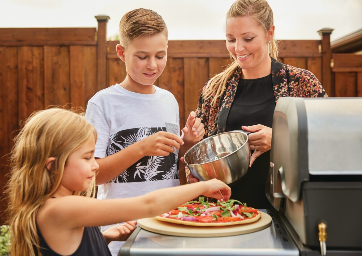 2 enfants et leur mere font de la pizza sur une pierre a pizza