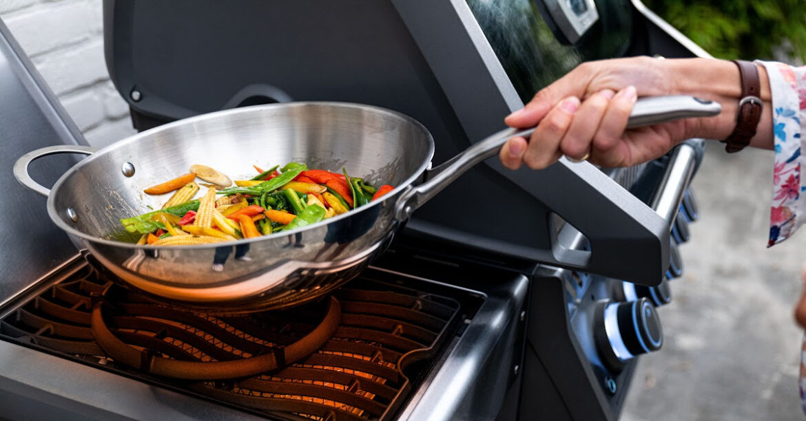 Des legumes grillent dans un wok sur un barbecue