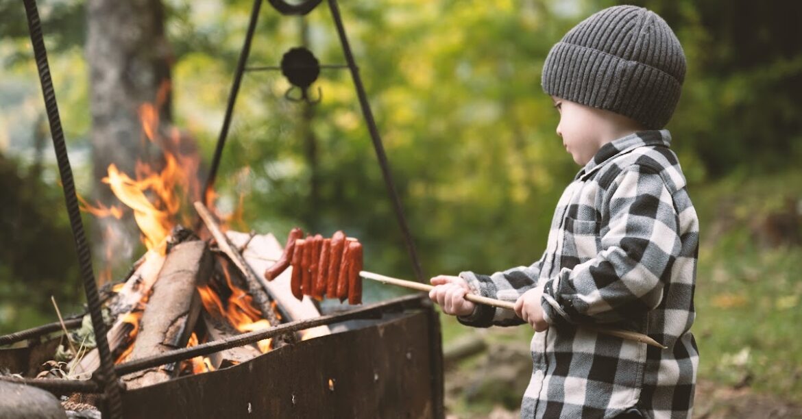 Un jeune garcon fait griller des saucisses sur un feu de camp